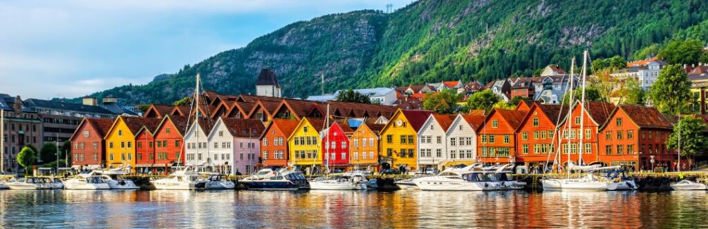Casas de colores junto a un fiordo en Noruega, rodeadas de montañas verdes y reflejos en el agua.