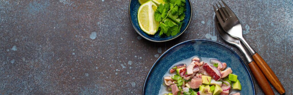 Image of a plate of ceviche accompanied by lime and cutlery