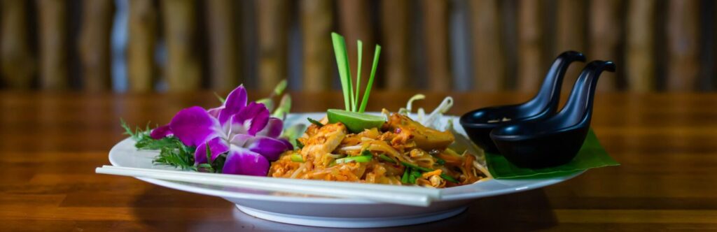 Pad Thai dish accompanied by purple flowers and spoons
