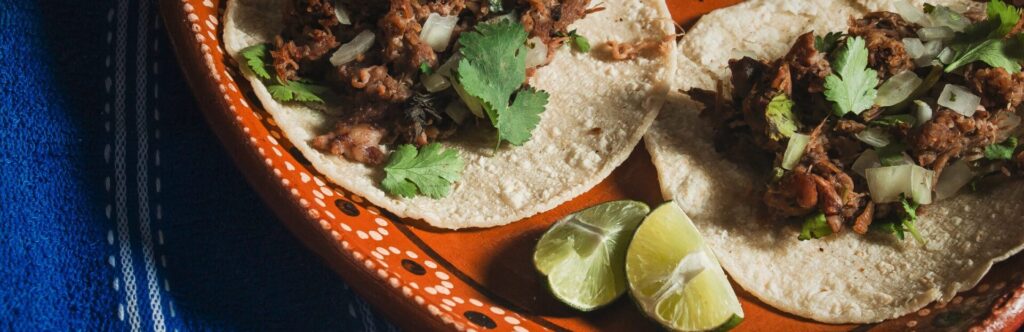 Image of two tacos accompanied by lime on a clay plate