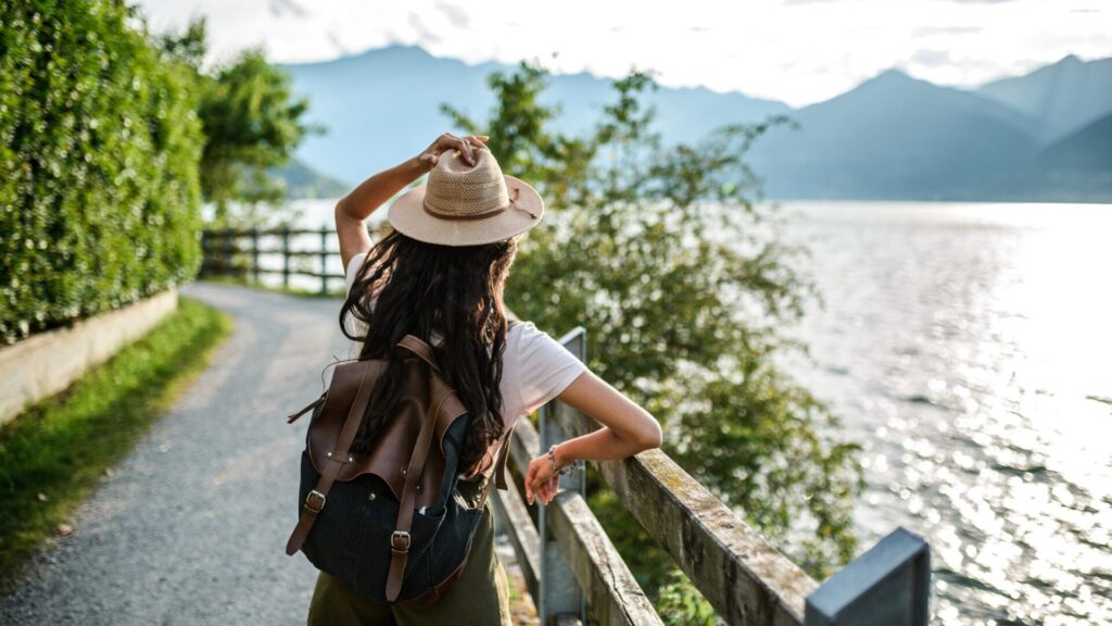 mujer joven paseando por un camino al borde de un lago con vistas montañosas