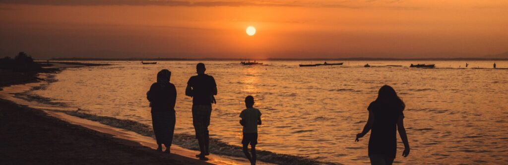 A family of four walking along the seashore with the sunset