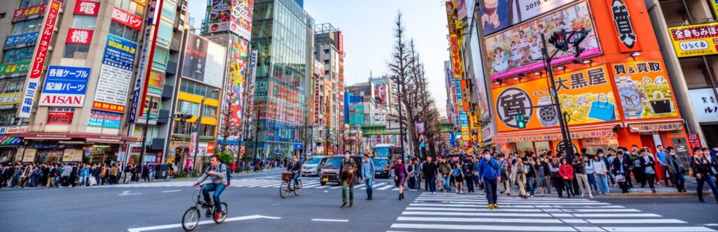 Image of Tokyo with buildings covered in colorful advertisements and crowds of people crossing the crosswalk