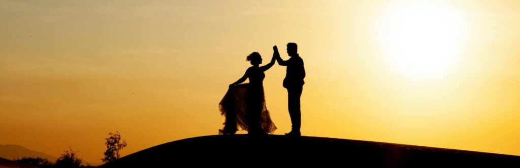 The silhouette of two people holding hands against the light at sunset