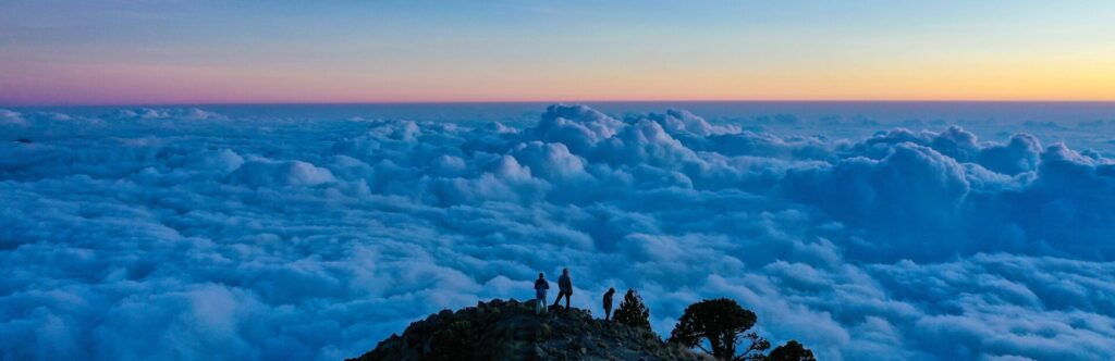Paisaje de una montaña con personas en lo más alto de esta con las nubes de fondo