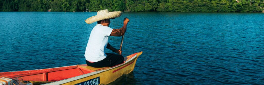 Hombre dirigiendo una barca en un lago con selva de fondo