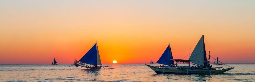 Varios barcos con el atardecer de fondo navegando en el mar