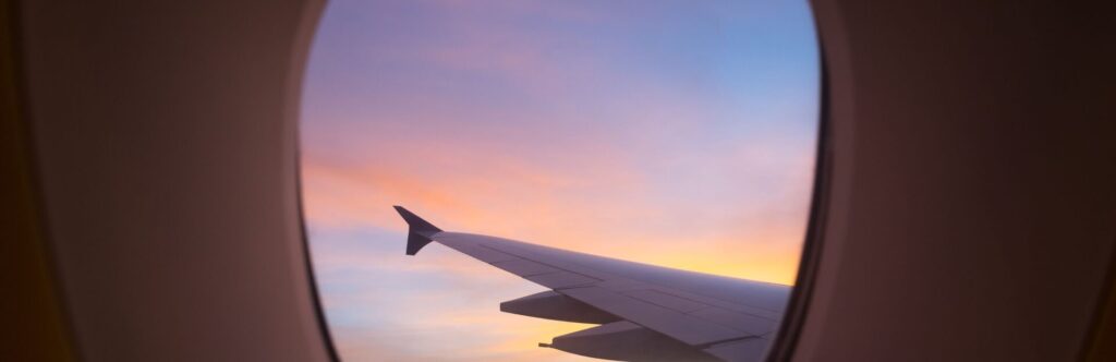 Foto desde una ventana del avión donde se ve el ala de este con el atardecer el fondo