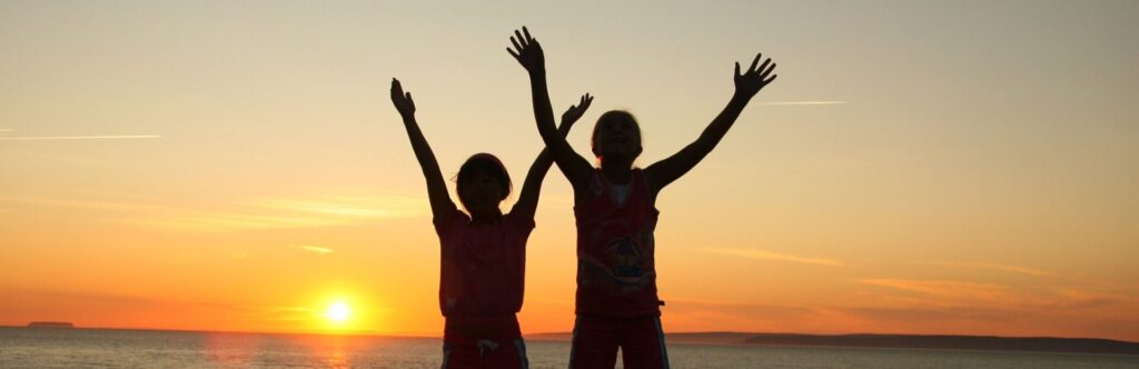 Dos personas levantando la mano con el atardecer de fondo