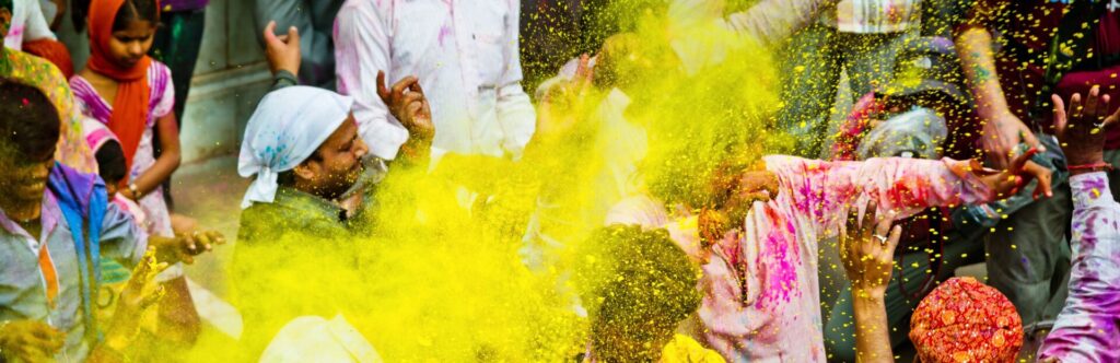 Imagen con personas de fondo tirándose polvos de colores, remarcando el color amarillo